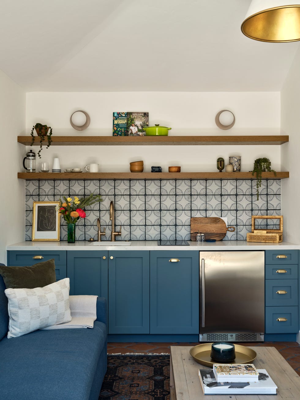 Eine kleine Küche verfügt über blaue Schränke mit goldenen Griffen, ergänzt durch eine minimalistische Arbeitsplatte und einen eleganten Kühlschrank aus Edelstahl