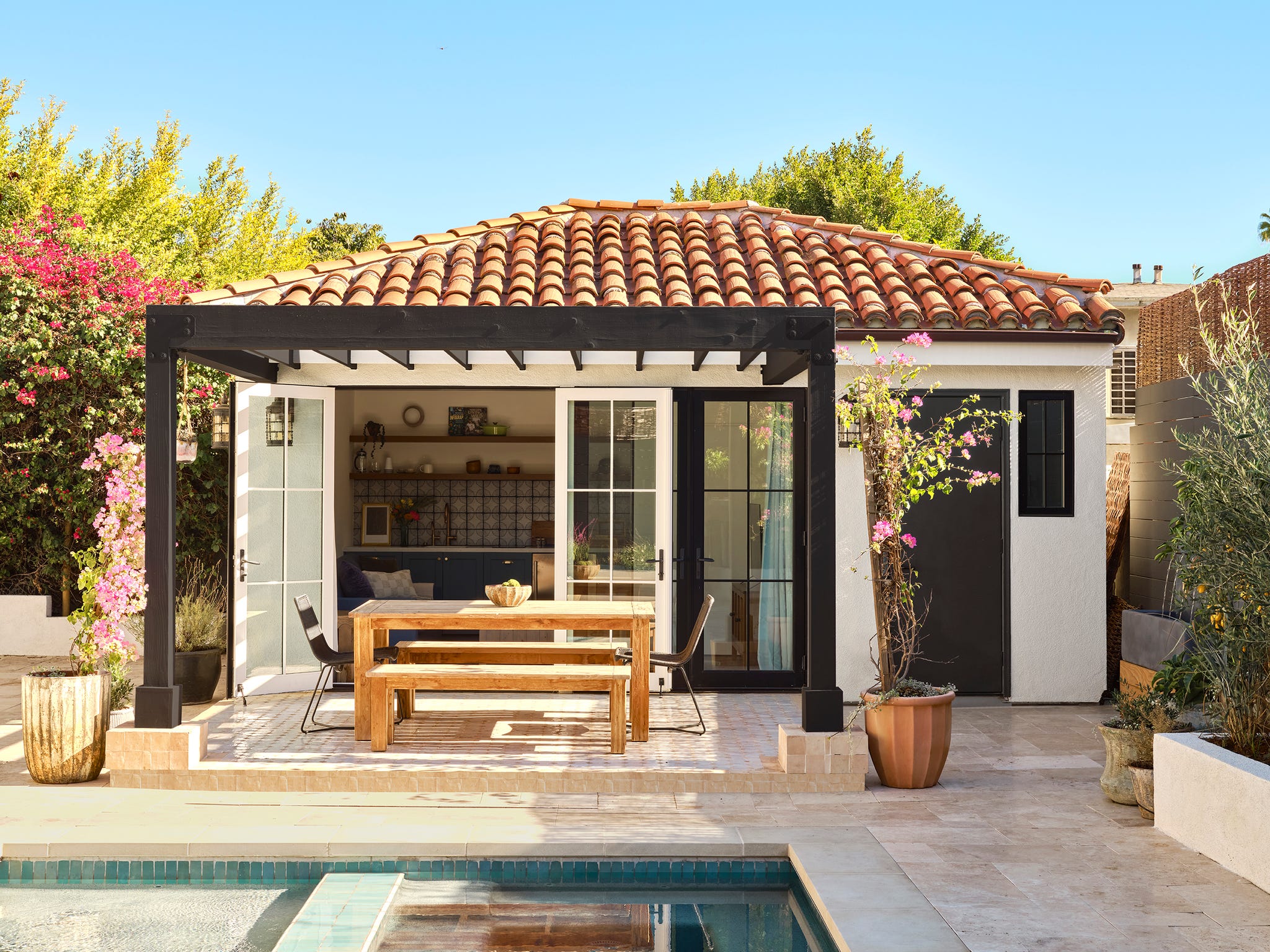Ein geräumiger Essbereich im Freien verfügt über einen Holztisch mit passenden Bänken, der unter einer schwarzen Pergola mit rosa Blumen geschmückt ist