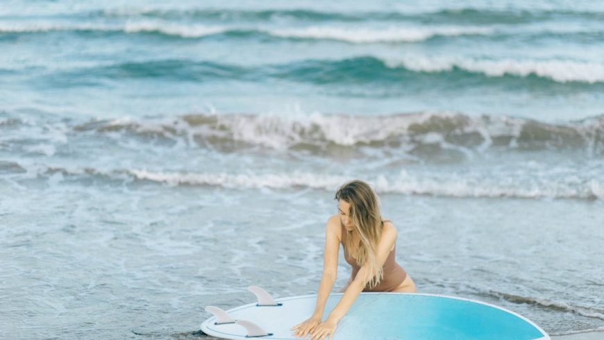 Frau im braunen Badeanzug und hält Hände über blaues Surfbrett, Meer, Ozean