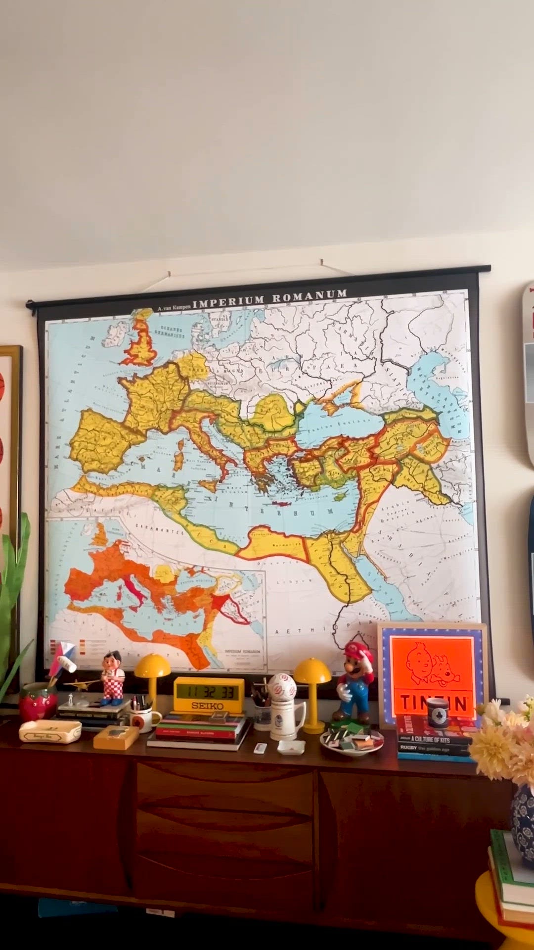 Ein stilvoll gekleideter Mann steht neben einer farbenfrohen modernen Umgebung mit einem Vintage -Kartendekor -Artikel und -büchern