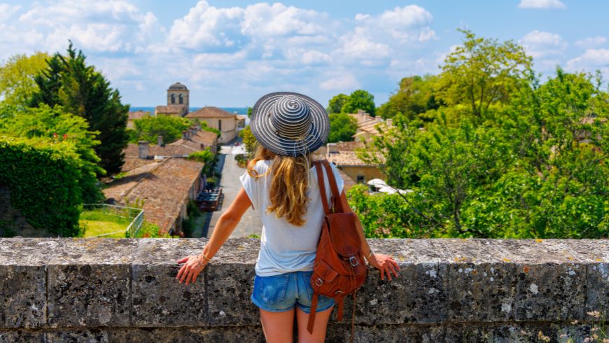 Eine junge Frau von hinten mit Blick auf eine malerische Landschaft mit einem kleinen, traditionellen Dorf in der Ferne, das für langsames und nachhaltiges Reisen fernab des Massentourismus steht.