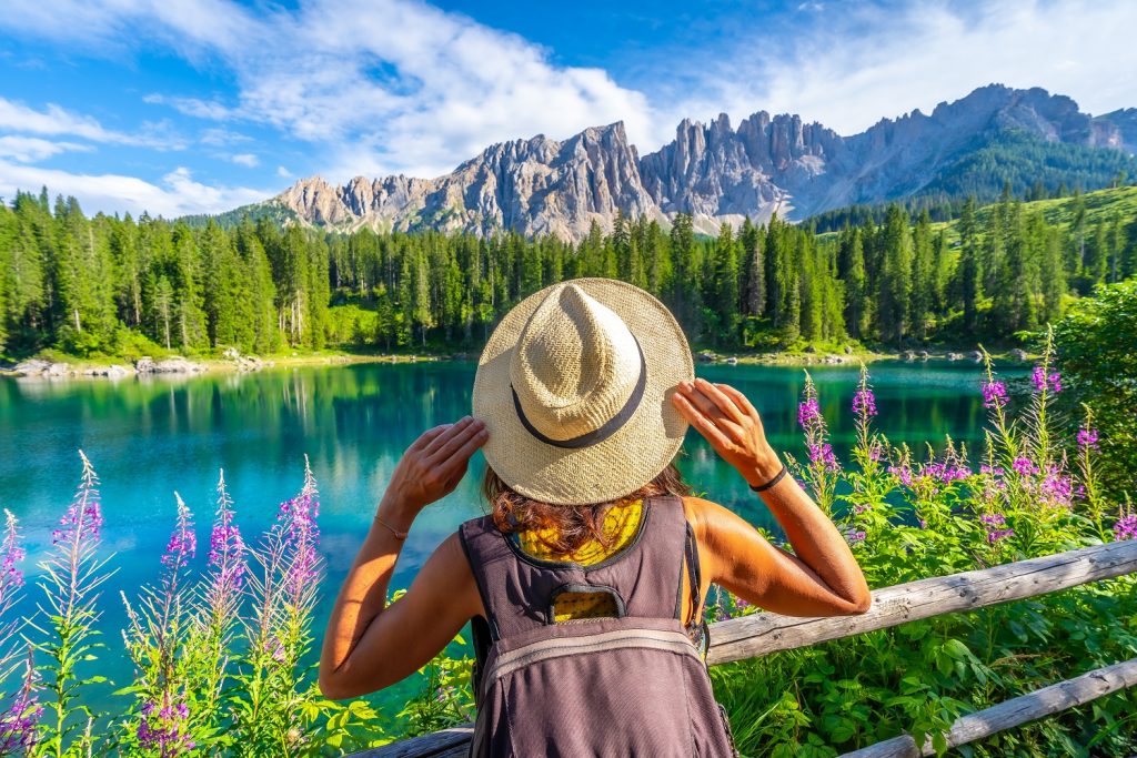 Touristin hält ihren Hut und genießt die atemberaubende Aussicht auf den Karersee und den Berg Latemar in den italienischen Dolomiten