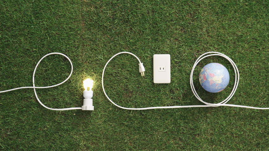 Glühbirne und Steckdosen auf einem grünen Rasen bilden das Wort „Öko“ mit dem Planeten Erde und symbolisieren nachhaltige Energie und Umweltbewusstsein.