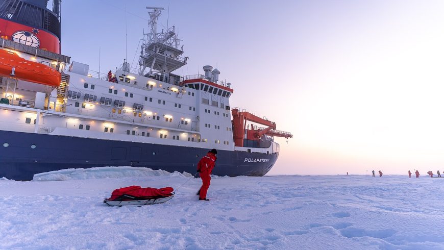 Wissenschaftler steht während einer wissenschaftlichen Expedition auf dem arktischen Meereis vor dem Forschungsschiff RV Polarstern