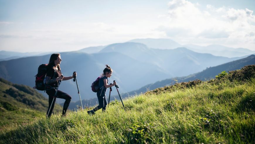 Zwei Mädchen wandern gemeinsam in den Bergen, umgeben von üppigem Grün und inmitten unberührter Natur.