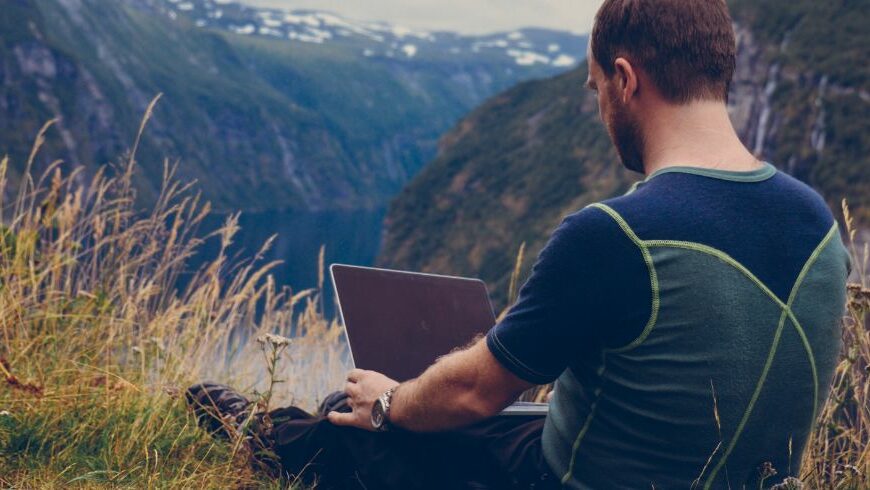 Remote-Mitarbeiter nutzt einen Laptop in den Bergen und kombiniert nachhaltiges Reisen mit flexiblem Arbeiten