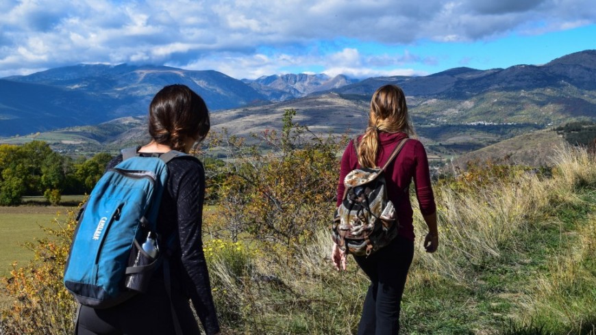 Zwei Mädchen wandern mit leichten Rucksäcken in den Bergen, umgeben von wunderschöner Naturlandschaft.